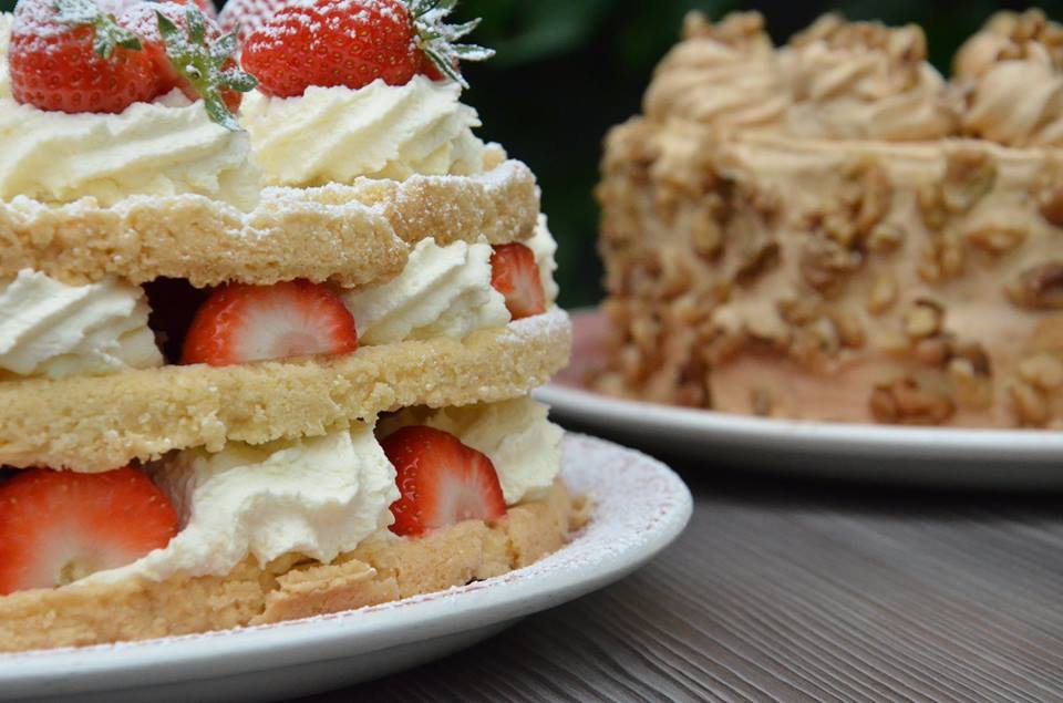A layered strawberry and cream shortcake beside a walnut and coffee cake