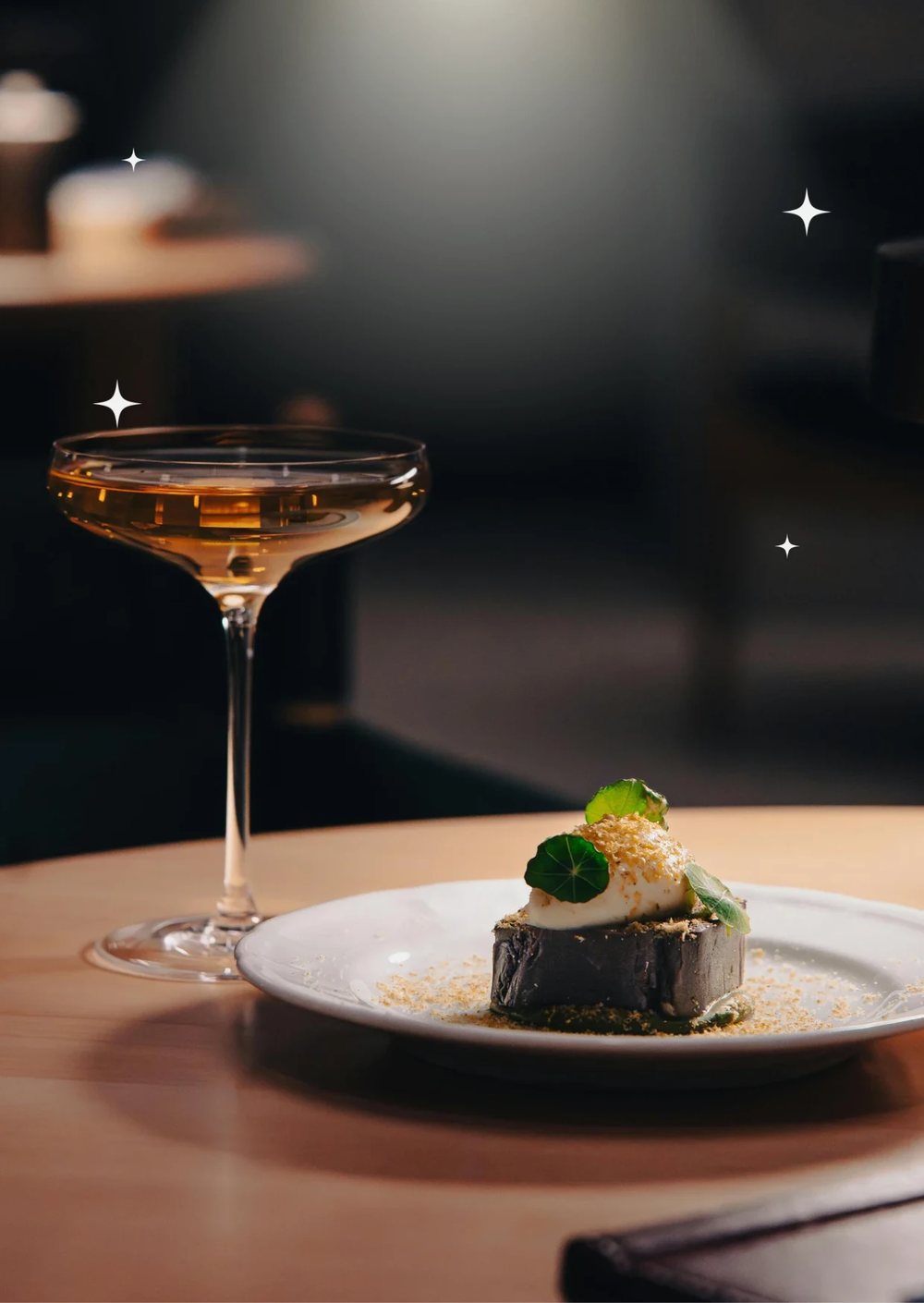 A coupe glass of wine beside a plated dessert garnished with nasturtium leaves, on a candlelit table